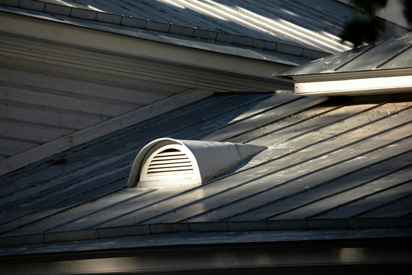 Louvered attic vent on a residential roofline in late-afternoon summer light, the exhaust half of an attic's airflow loop.