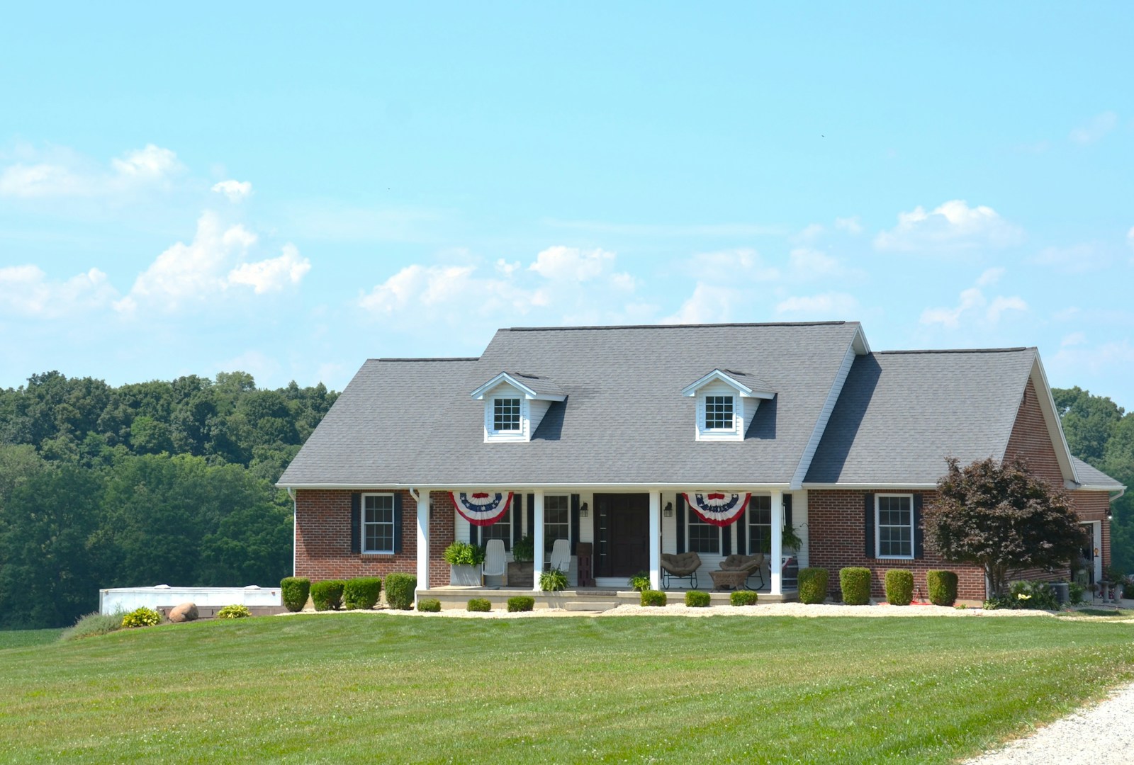 Sunlit brick home with a green summer lawn, the kind of exterior mid-summer pests quietly probe for a way inside.