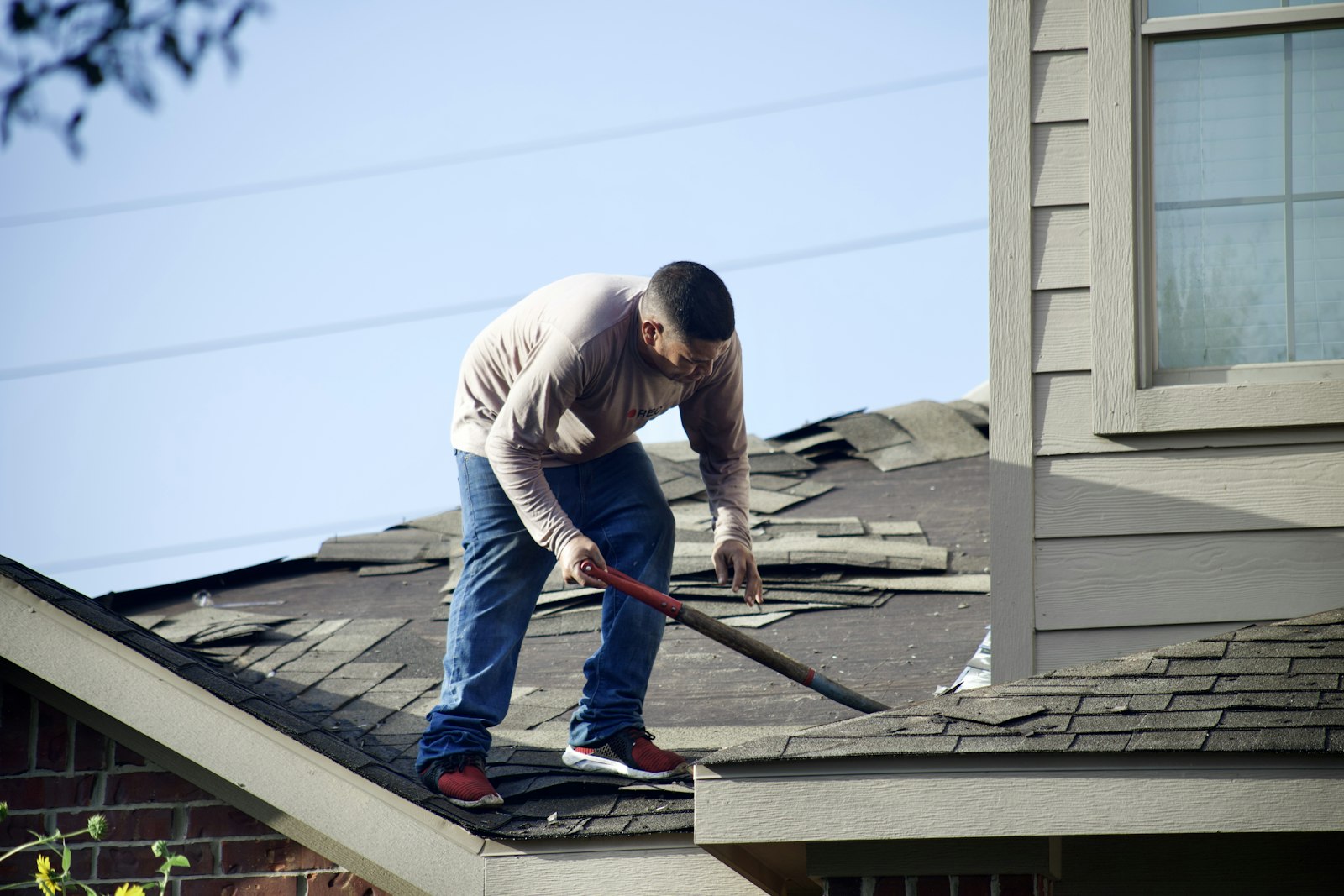 A roofer clearing storm-damaged asphalt shingles off a North Texas home after a hailstorm.