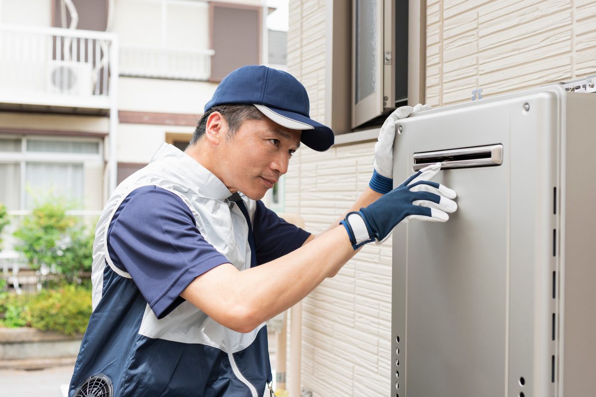 A technician carefully servicing an outdoor tankless water heater